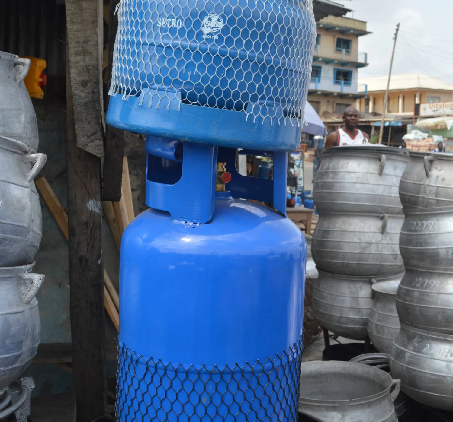 A blue LPG cylinder beside a stack of large aluminium catering pots